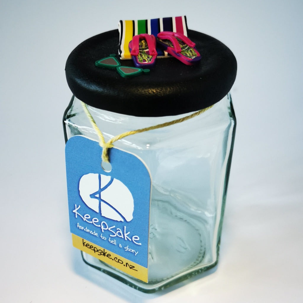 185ml glass hexagonal  jar and lid hand-decorated in New Zealand, with  an air-tight lid decorated with polymer clay beach towel and jandals . Ready to be filled with fudge, sweets or other treasures.