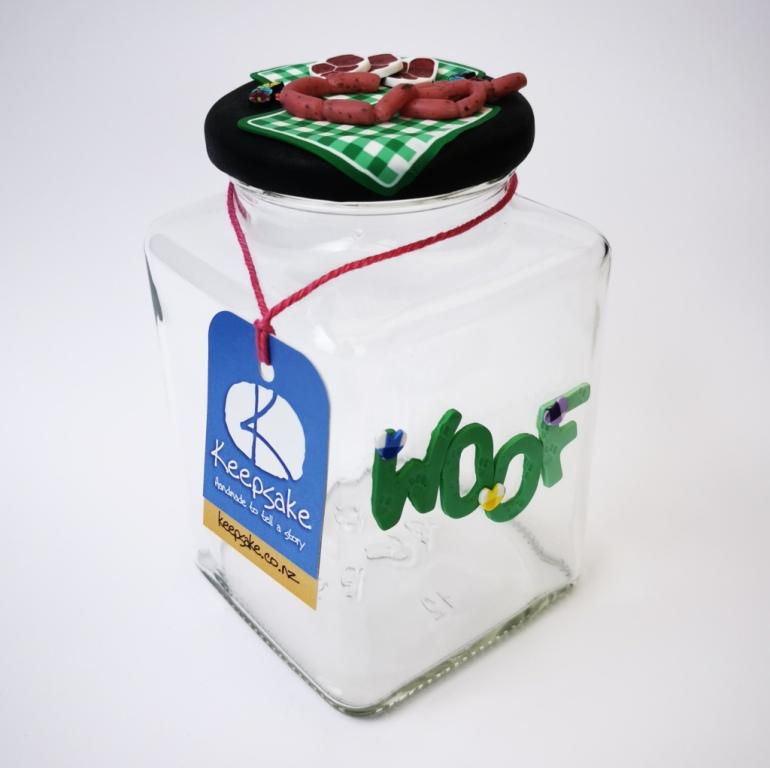 Square Dog glass treat Jar hand-decorated in New Zealand,  with  green WOOF on the front and polymer clay decorated air-tight lid, including a green tablecloth, miniture sausages and steak as a gift for that special dog