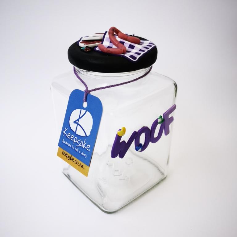 Square Dog glass treat Jar hand-decorated in New Zealand,  with  purple WOOF on the front and polymer clay decorated air-tight lid, including a purple tablecloth, miniture sausages and steak as a gift for that special dog