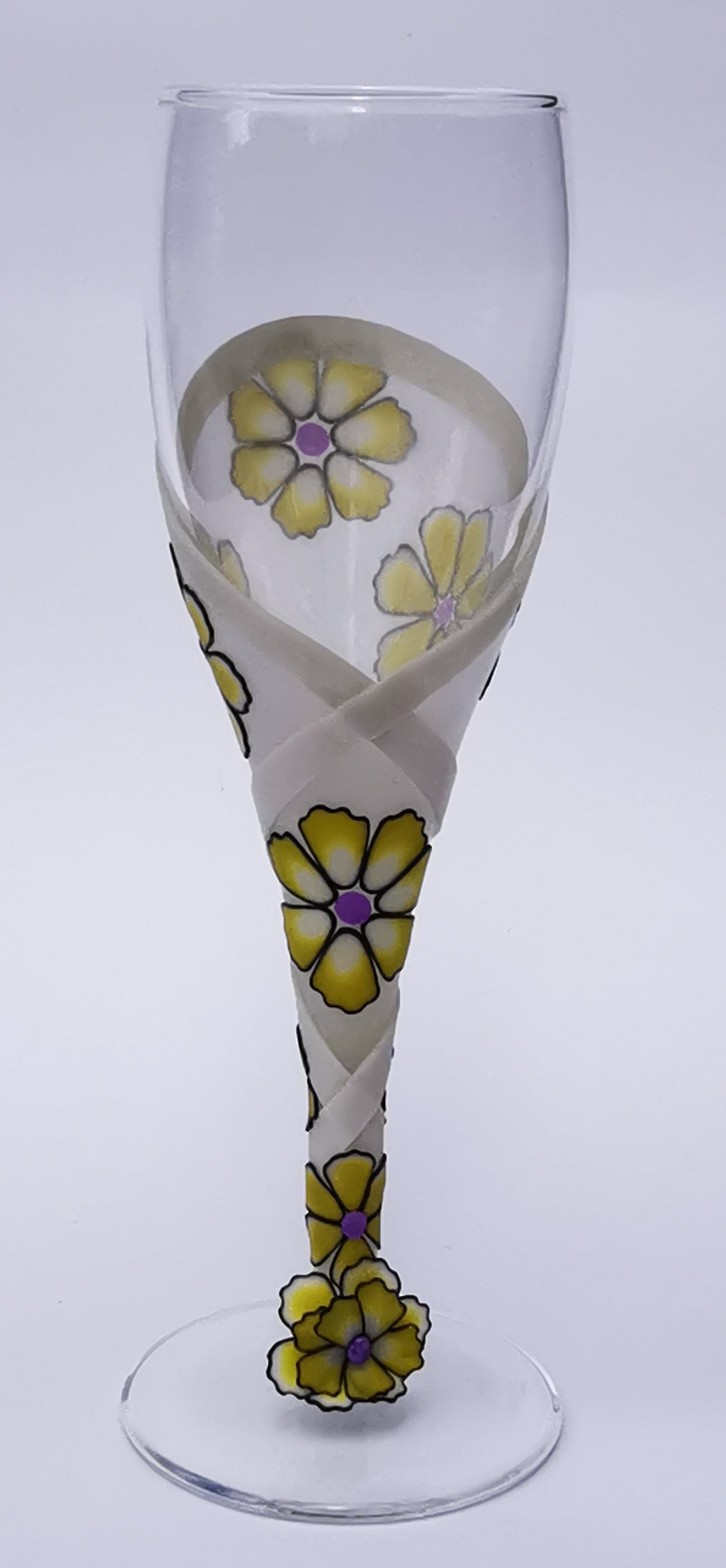 Decorated champagne flute with coloured frilly flowers bordered in black with wound ribbon and flower at base
